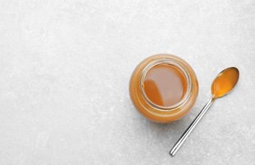 Jar with tasty caramel sauce and spoon on light background