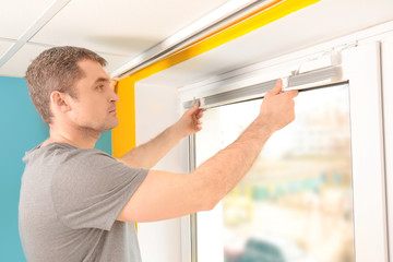 Young man installing window shades at home