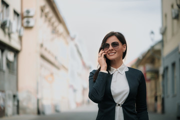 Fototapeta premium Young Woman Walking the City Talking to Someone on her Mobile Phone While Looking Into the Distance with Happy Facial Expression