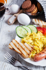 Hearty and traditional breakfast, scrambled eggs and milk with grilled pork, vegetables, tomato, cucumber, toast, juice and black coffee on a white wooden background
