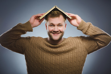 young man reading a book and smiling on grey background