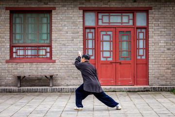 un homme chinois habillé en noir, s'entraine au tai chi seul dans un décors asiatique
