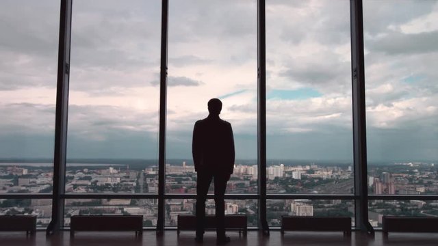 Rear view of man in formal suites who stand in front of panoramic window with city view. a man stands in front of big panoramic wiindow view from back.
