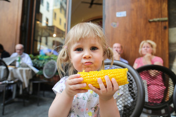 A cute young blond girl eating a bolied corn. 