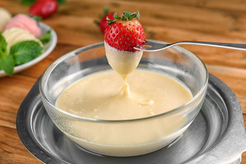 Fork with fresh strawberry dipped in white chocolate fondue, closeup