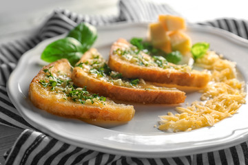 Plate with tasty garlic French bread slices and striped napkin