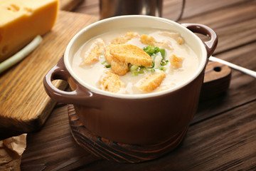 Delicious beer cheese soup with croutons and onions on table