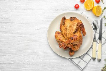 Plate with roasted beer can chicken on wooden background