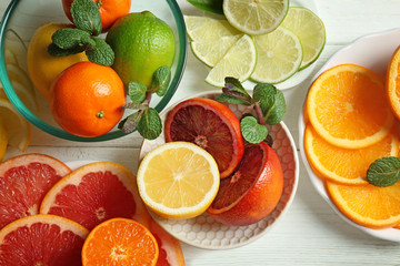 Plates with different citrus fruits on white wooden background