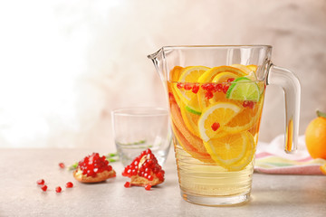 Glass jug with refreshing citrus fruits cocktail on light background