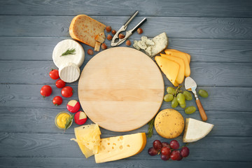 Variety of cheese and nuts around cutting board on wooden background