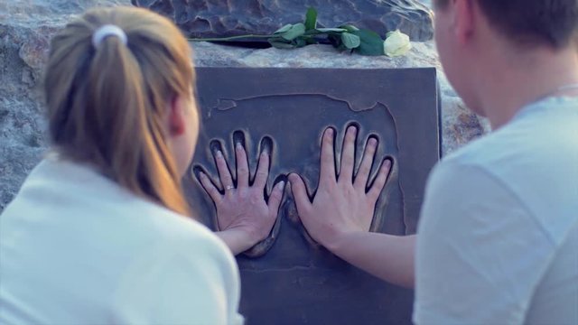 The couple puts hands to the monument couple in love on date stands at the monument. to attach the arm to the monument