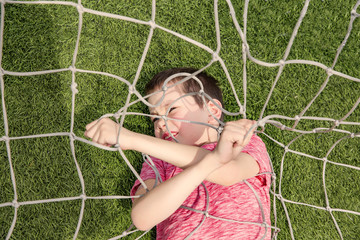 boy tangled in soccer net. The kid lying on the football field and tries to get out of the net. Top...