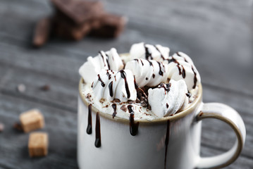Cup of cocoa with whipped cream, marshmallows and chocolate syrup on wooden table
