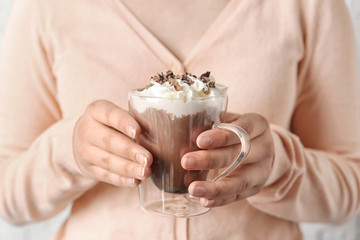 Woman holding glass cup of cocoa drink with whipped cream in hands