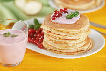 Plate with delicious pancakes and glass of yogurt on yellow table