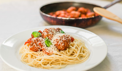 Spaghetti pasta with meatballs in tomato sauce, basil leaves, and cheese against white background