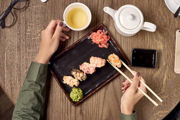 Flatlay. Closeup of woman hands with bamboo chopsticks eating sushi with green tea.