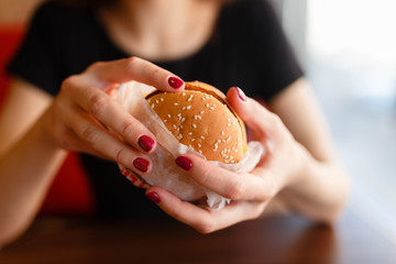 Young girl holding in female hands fast food burger, american unhealthy calories meal on background, mockup with copy space for text message design, hungry human with grilled hamburger front view