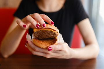 Young girl holding in female hands fast food burger and shows what he is made of, with copy space for text message or design, hungry human with grilled hamburger front view.