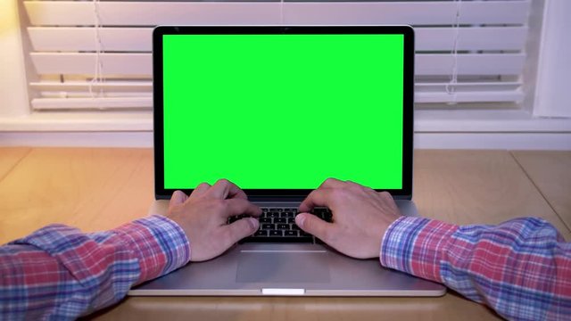 A man uses a laptop in his home office. Green screen for your custom screen content.	