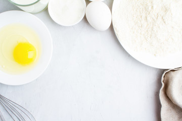 Flour, eggs, sugar, milk, rolling pin and whisk on a white background close-up.