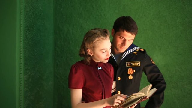 A man and a girl in retro style read a book on the balcony. The models are posing for a retro-style photo shoot.