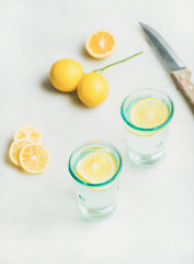 Morning detox lemon water in glasses and fresh lemons over light grey marble background, selective focus, vertical composition. Clean eating, weight loss, healthy, detox, dieting concept