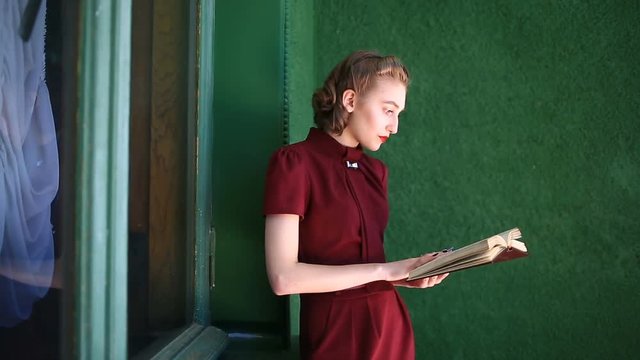 Happy pin-up girl in a retro style dress. Girl with positive emotions. Model poses for a photo shoot in retro style. She is reading a book on the balcony