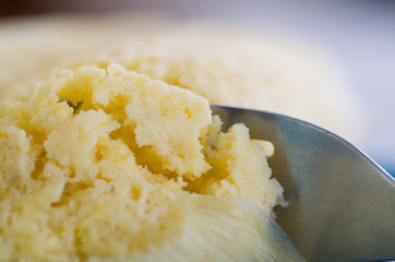 A close up from a metallic fork slicing a piece of humita over a blue dish