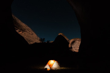 Glowing tent at night in canyon under stars