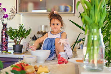 A cute little girl sits on a table and trying to cook.