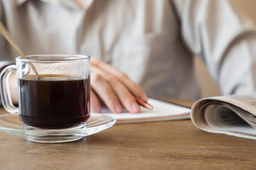Man drinking black coffee and writing something in the note-book at the table in the cafe at lunch time. Coffee break.