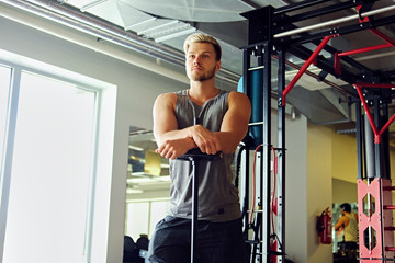 Sporty male in sportswear holds barbell over TRX stand background in a gym club.