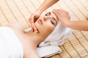 Beautiful, young and healthy woman on bamboo mat in spa salon having face massage. Spa, health and healing concept.