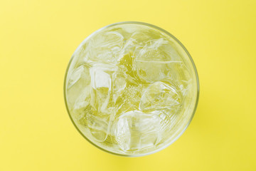 glass of soda with ice blocks isolated on yellow background, top view