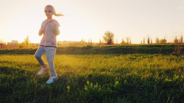 A 6 year old girl is doing exercises on a green meadow at sunset