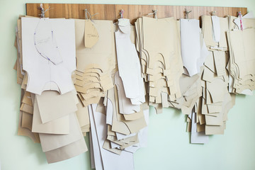 Many paper brown patterns for sewing clothes for babies and newborns of different sizes hanging on wall in sewing factory interior. Horizontal color photo.
