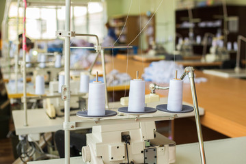 Closeup of three big bobbins with thin white thread on working professional sewing machine.  Horizontal color photo.