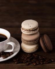 Set of coffee macaroons with a cup of coffee on dark wooden background. Cream macaroons