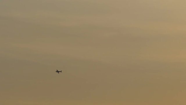 A small plane is passing the orange sunset sky at the distance .
