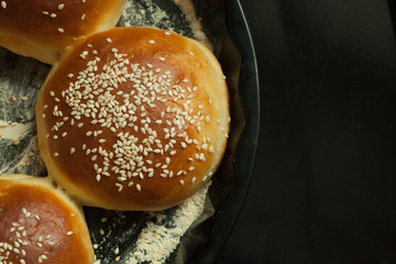 buns for burgers with sesame in a baking form on black background, copy space, top view