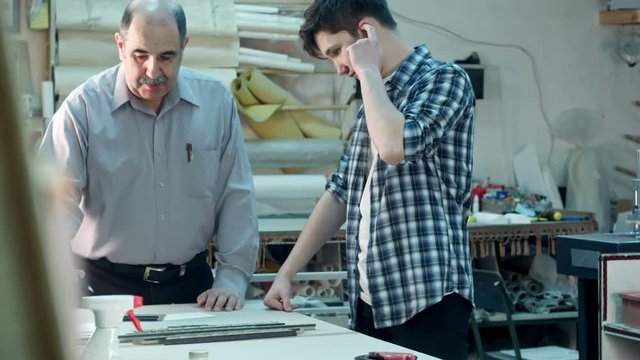 Senior male worker instructing young trainee how to construct a frame behind the desk in frame workshop