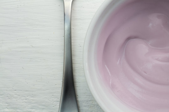 Yogurt close up view form top - Natural rasberry flavored yoghurt in white bowl on wood table
