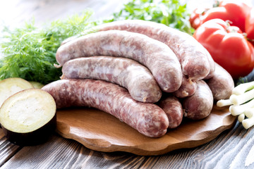 Raw sausages lying on wooden board Fresh vegetables and greens Tomato Parsley
