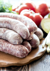 Raw sausages lying on wooden board Fresh vegetables and greens Vertical photo