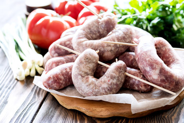 Raw sausages lying on wooden board Fresh vegetables and greens Onion Tomato Parsley