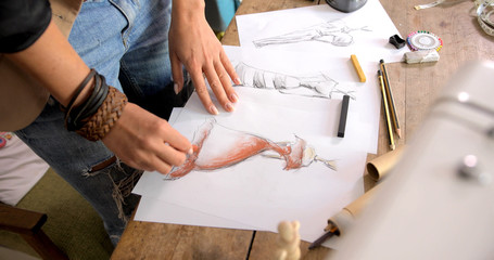 Crop faceless shot of female tailor standing near table in parlour and drawing sketches. 