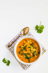 Healthy diet carrot cream soup with chickpeas in white bowl on the wooden table.