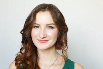Fototapeta premium Young brown-haired girl portrait. Fresh makeup. White background. Studio photo. Happy elegant lady. Curled hairstyle
